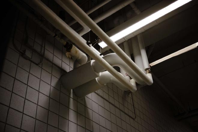 Pipes and a fluorescent light intermingled against the ceiling, casting shadows.