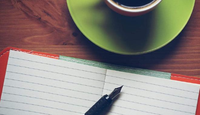 a fountain pen resting on a notepad with coffee on a desk