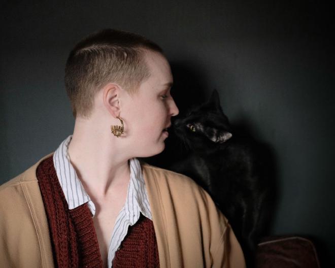 a woman with shaved hair touching noses with a black cat