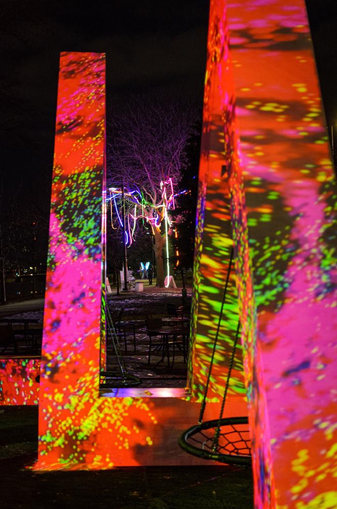 A sculpture in the shape of an &lsquo;M&rsquo; with a variety of colors, patterns, and shapes being project onto it. It&rsquo;s striking against the night sky.