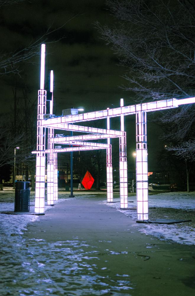 an angular structure that makes its way along and over a sidewalk, each piece and pillar contains LED lights that change color