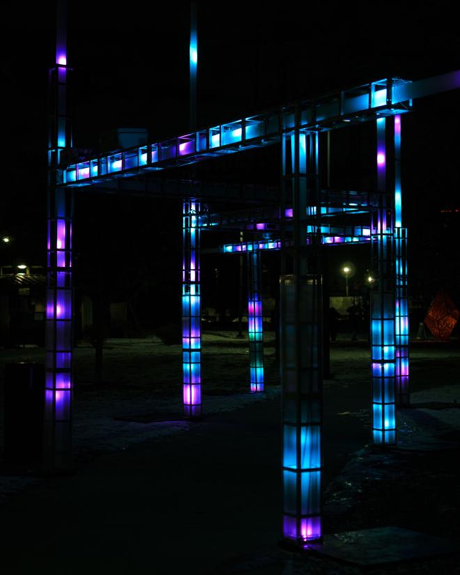 an angular structure that makes its way along and over a sidewalk, each piece and pillar contains LED lights that change color