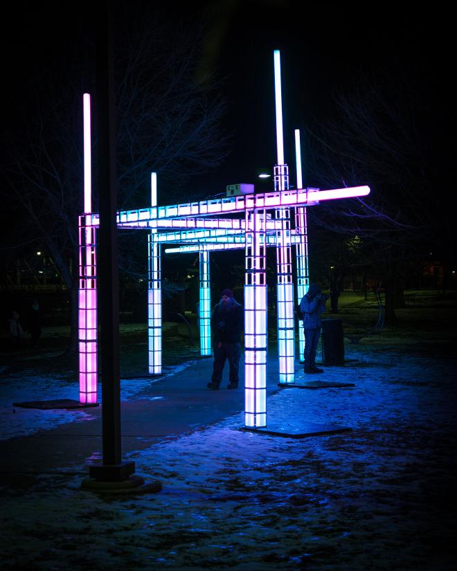 an angular structure that makes its way along and over a sidewalk, each piece and pillar contains LED lights that change color